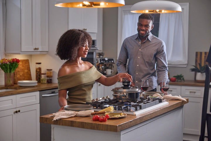 A couple cooking together with a covered A by AMC pot on the stovetop.