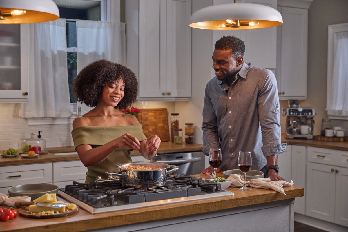 A couple cooking with A by AMC stainless steel cookware in a home kitchen.