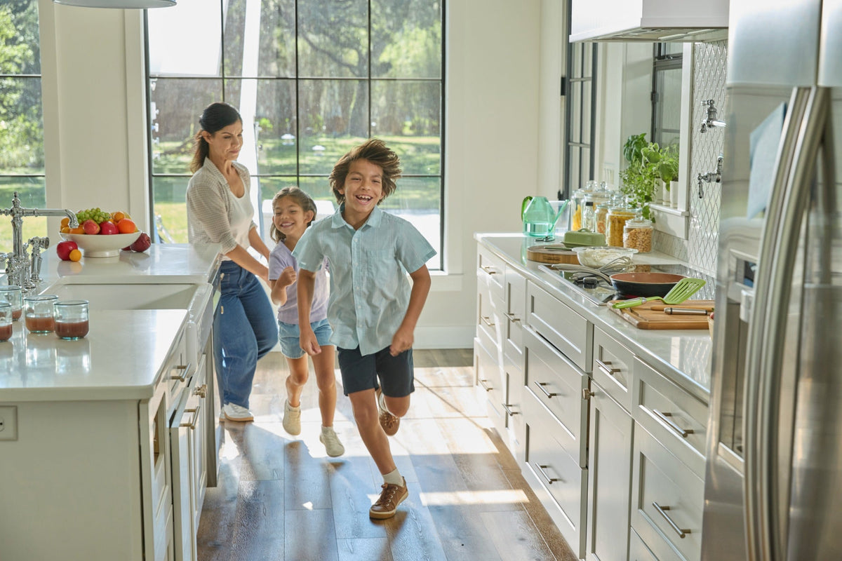 Children running through a bright family kitchen, a pan on the cooktop nearby.