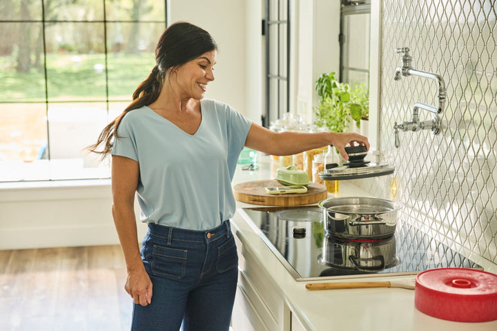 Woman lifting the lid off an A by AMC pot on an induction cooktop.