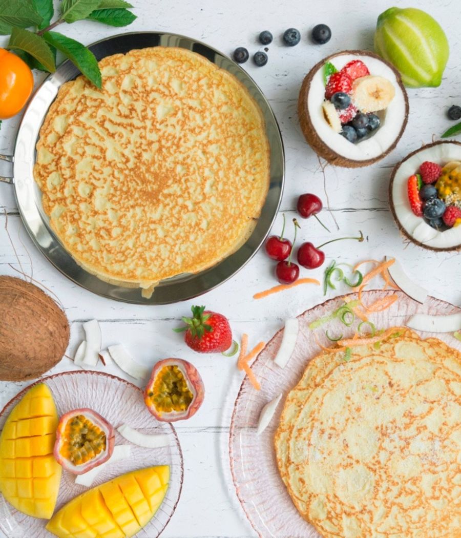 A large golden crêpe in the oPan, with fresh fruit on the table
