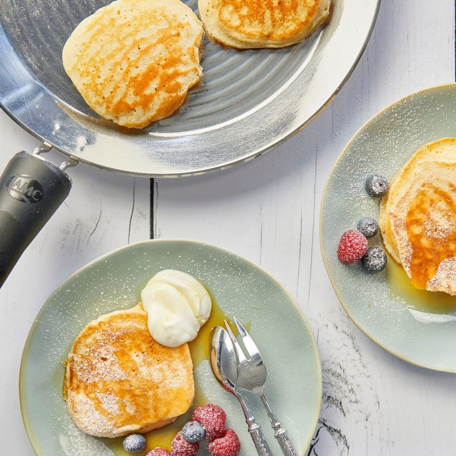 Fluffy pancakes in the oPan, with berries and cream on the table